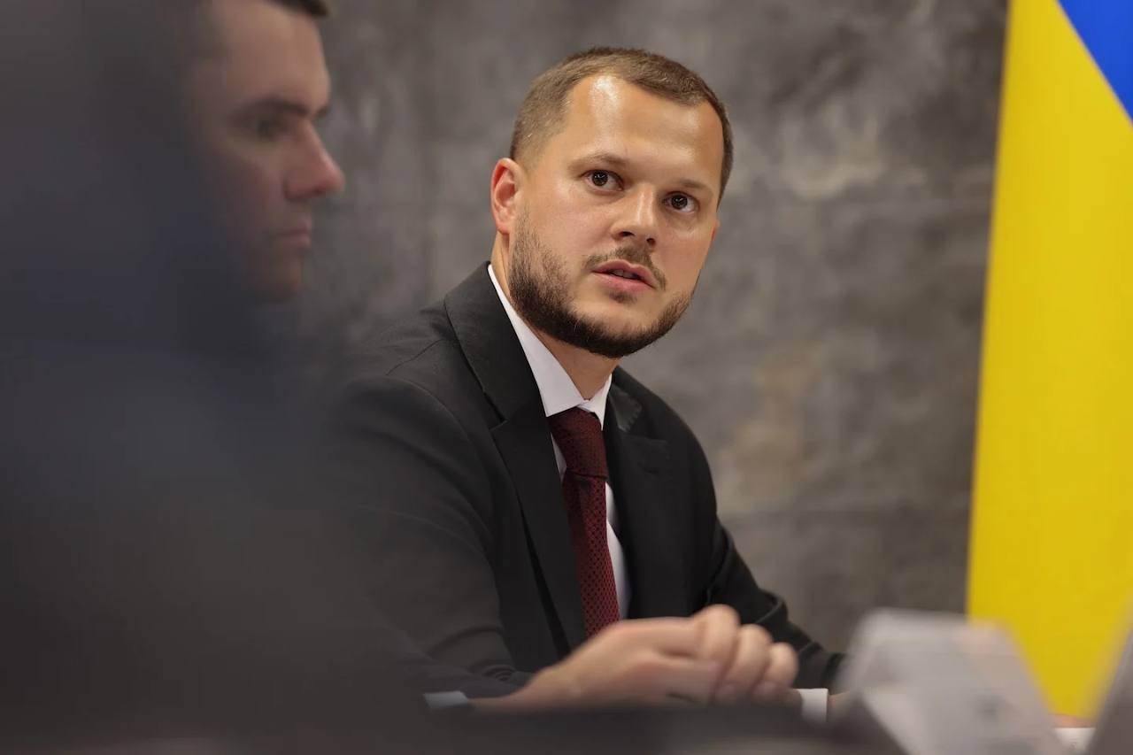 Учасник наради у чорному костюмі та бордовій краватці виступає на фоні державного прапора під час обговорення енергетичної стійкості регіонів.