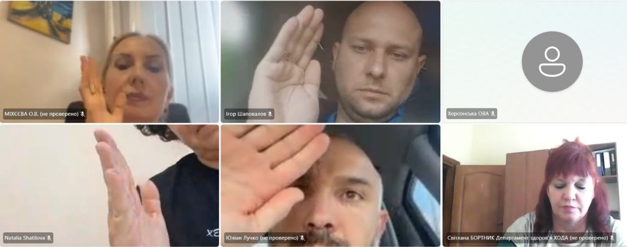 Скриншот онлайн-наради гуманітарного штабу при Херсонській ОВА з шістьма вікнами учасників на екрані. Більшість присутніх на відеозв'язку одночасно тримають підняту руку вгору під час голосування. Серед них — директор Департаменту соціального розвитку Херсонської ОДА О. В. Міхєєва (верхнє ліве вікно), заступник начальника Херсонської РВА Юліан Лучко (нижнє центральне вікно), Ігор Шаповалов та Наталія Шатілова. У правому нижньому кутку засідання слухає Світлана Бортник із Департаменту здоров'я ХОДА.