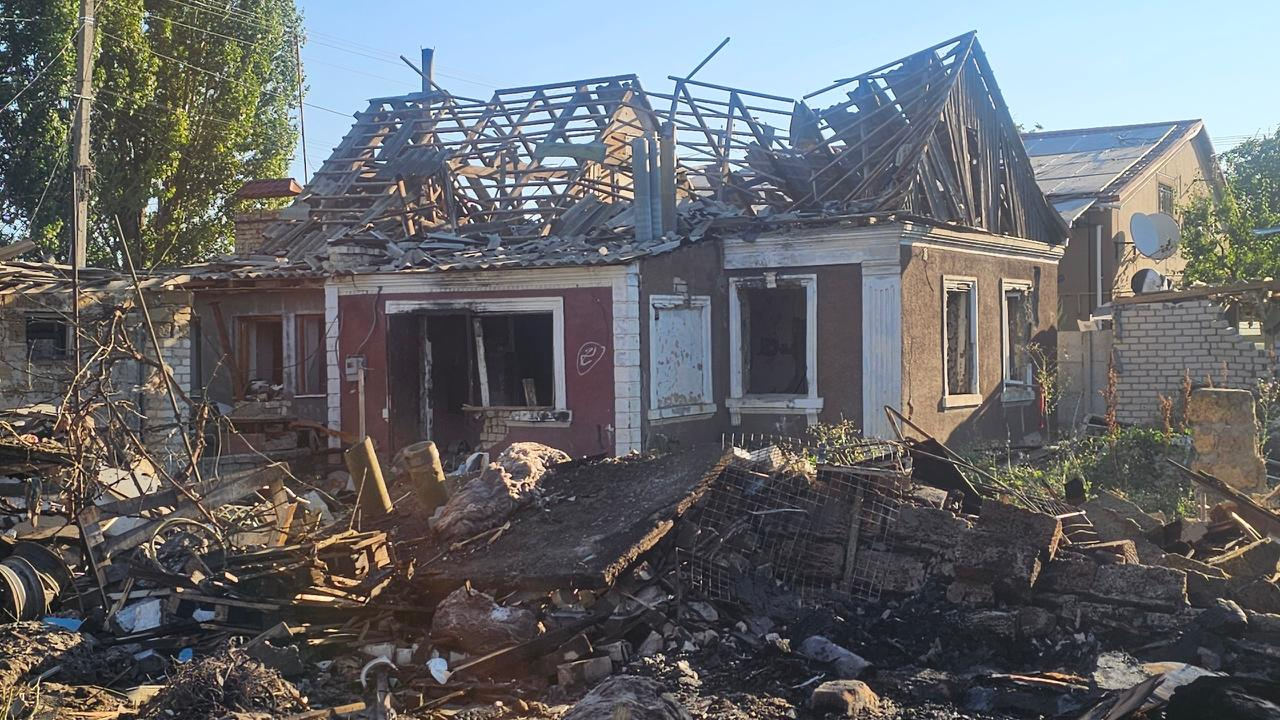 Наслідки нічної атаки «Шахедів» на Херсон: зруйнований вщент приватний будинок у Центральному районі. У будівлі повністю знищено покрівлю — видно лише обгорілий дерев'яний каркас даху, вікна вибиті, а стіни понівечені. На передньому плані лежить купа обвугленого будівельного сміття та уламків.