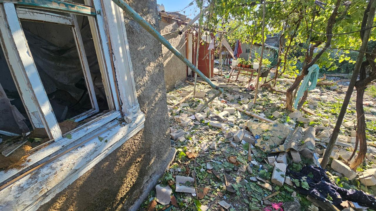 Засипане цеглою та будівельним сміттям подвір'я приватного будинку в Херсоні з вибитим вікном, пошкодженою стіною та понівеченими вибухом зеленими насадженнями.