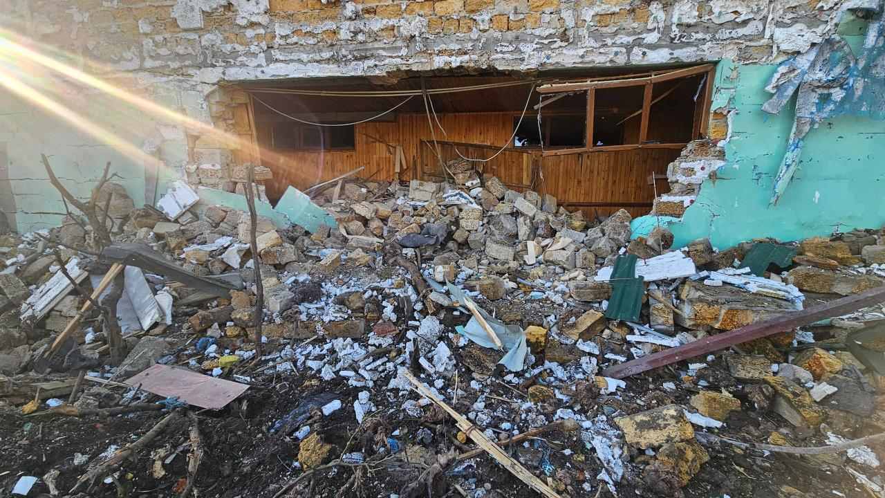 Частково зруйнована вибухом стіна капітальної будівлі з великим проломом, через який видно дерев'яну обшивку всередині, та великою купою уламків цегли й каміння на землі.
