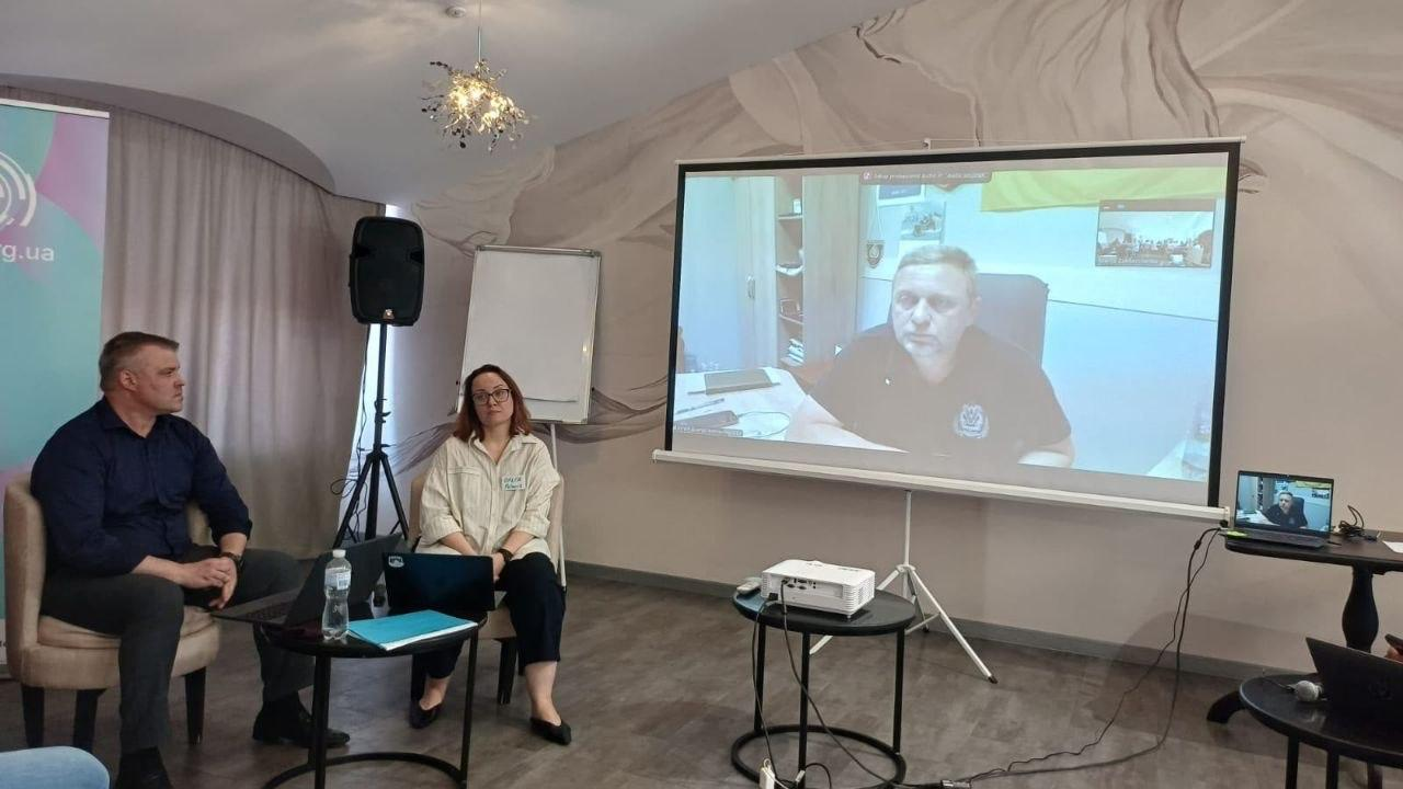 Директор Департаменту розвитку економіки ХОДА Артем Мішин та керівниця команди «Програми Polaris» Ольга Шубіна сидять біля великого екрана, на якому через відеозв'язок виступає перший заступник начальника Херсонської ОВА Дмитро Бутрій під час презентації Стратегії розвитку області.