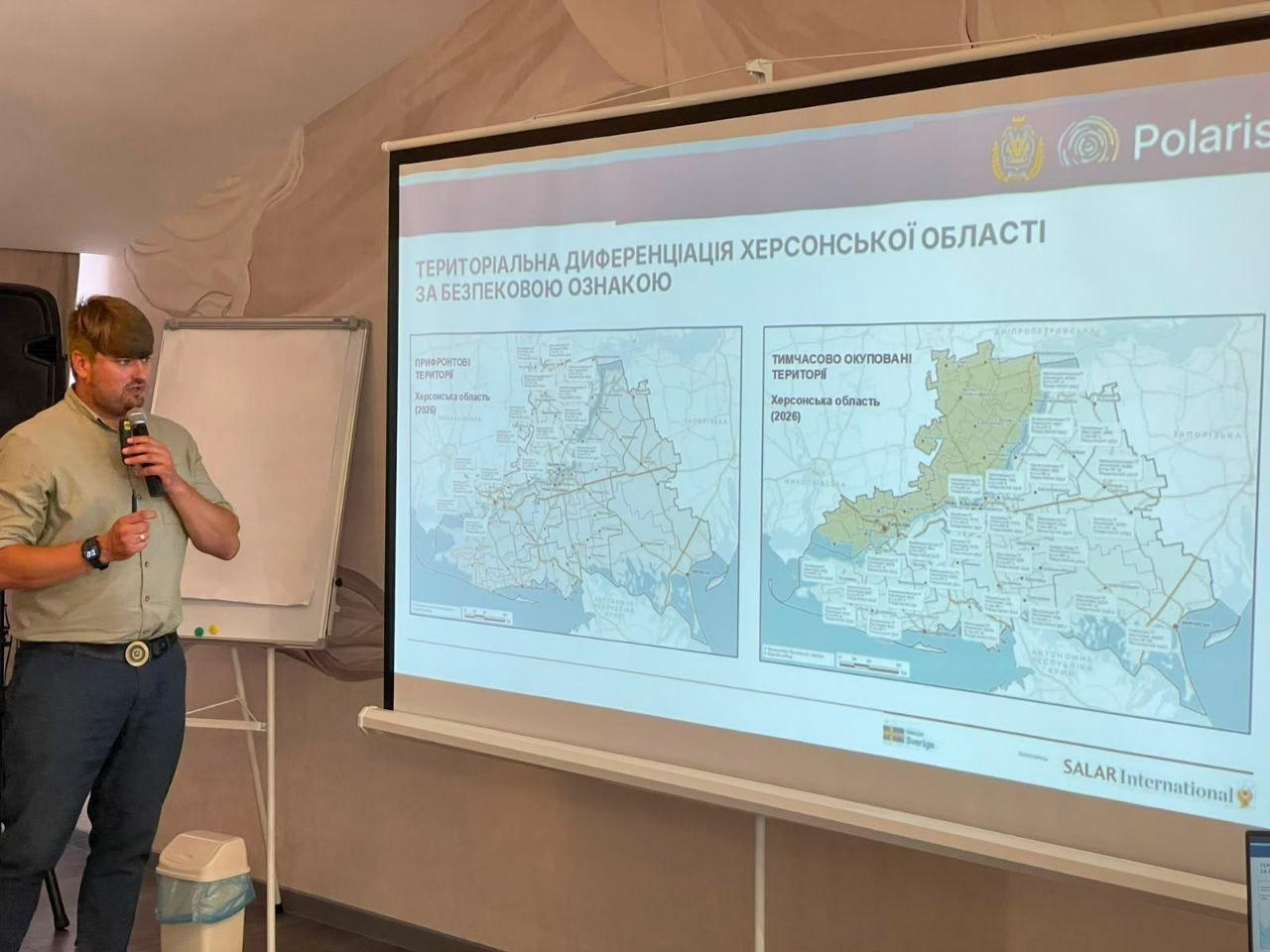 Чоловік з мікрофоном виступає біля великого екрана, на якому представлено слайд програми Polaris із мапами та заголовком «Територіальна диференціація Херсонської області за безпековою ознакою».
