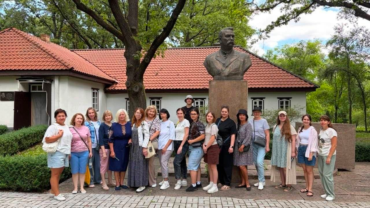 Група переселенців з Херсонщини та працівників Верхньорогачицької СВА позує для спільного фото біля погруддя Івана Карпенка-Карого на території державного заповідника-музею «Хутір Надія» під час краєзнавчого візиту від клубу «РІКА».