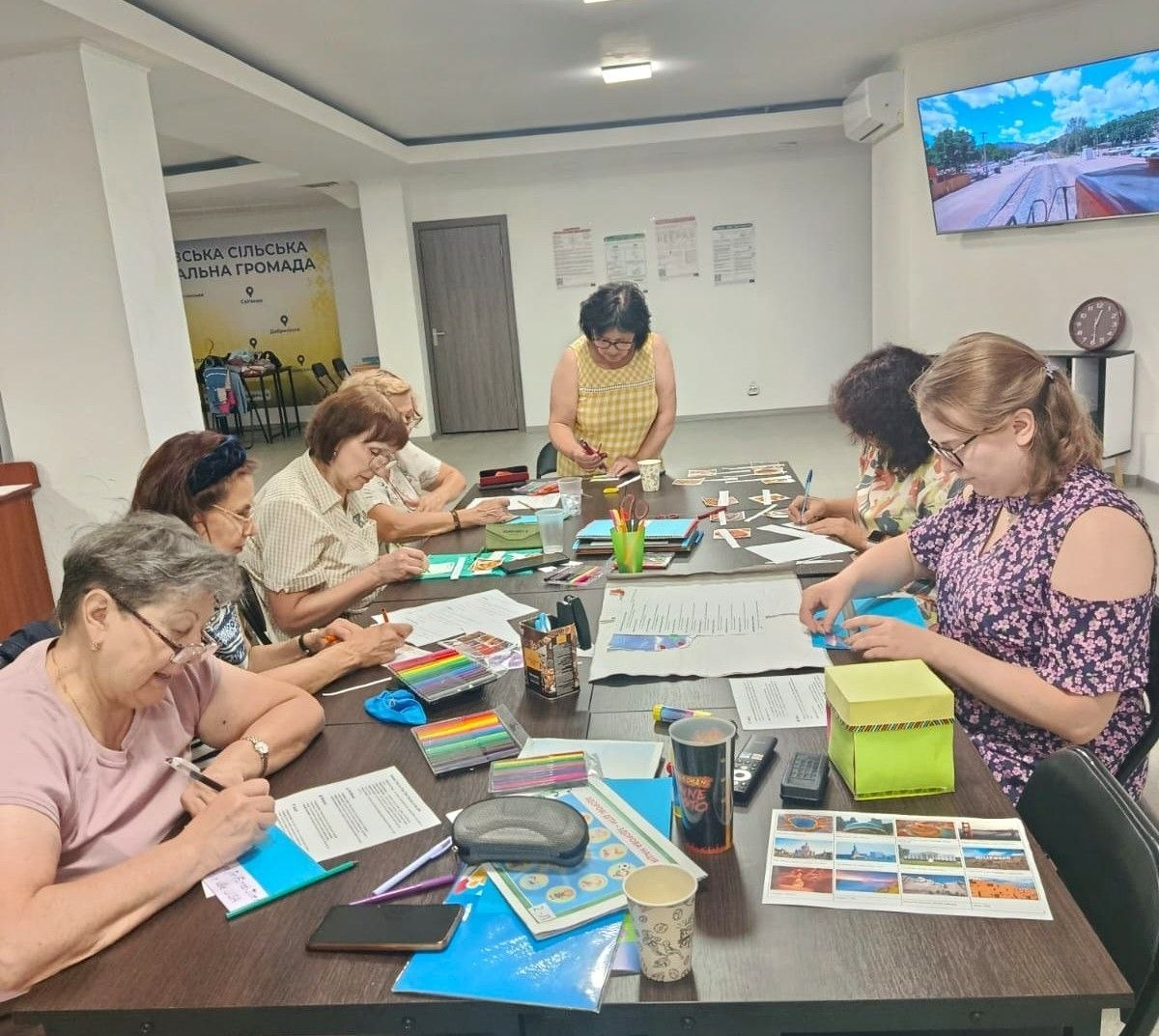 Учасниці заняття з англійської мови в Координаційному центрі «Вільні разом» у Черкасах сидять за столом і спільно створюють навчальний лепбук «Подорожі регіонами США».