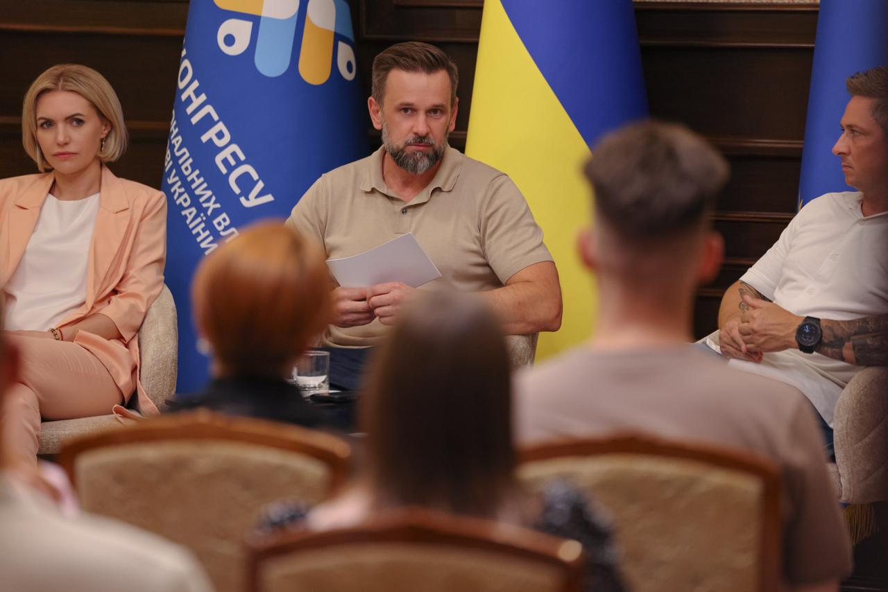 Засідання Палати регіональних молодіжних конгресів. У центрі за столом сидить Заступник Керівника Офісу Президента України Віктор Микита. Ліворуч від нього на передньому плані спиною до камери сидить рудоволоса керівниця Молодіжного конгресу Херсонщини Катерина Саваєва, яка слухає виступ. На задньому плані ліворуч сидить жінка у персиковому костюмі, а праворуч — чоловік у білій футболці на тлі прапора України та синього банера Конгресу.