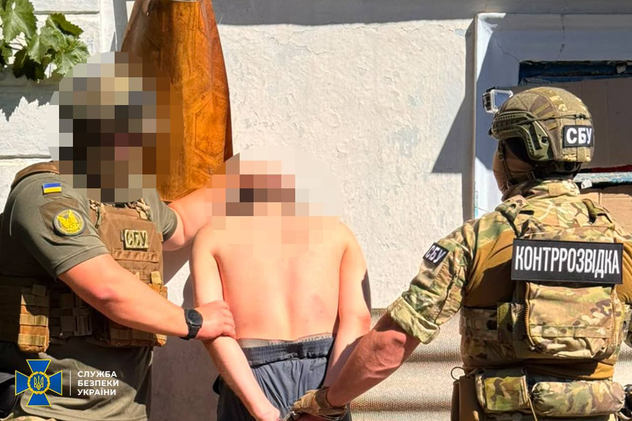 Двоє озброєних співробітників СБУ та контррозвідки у камуфляжній формі, плитоносках та шоломах затримують у Херсоні підозрюваного в інтернет-агітації чоловіка з голим торсом. Ліворуч оперативник тримає фігуранта за плече, праворуч спиною до камери стоїть другий правоохоронець у жилеті з написом «КОНТРОЗВІДКА» та шевроном «СБУ» на шоломі. Голова та обличчя затримуваного, а також обличчя бійця ліворуч повністю розмиті в інтересах слідства. У нижньому лівому кутку розміщено офіційний логотип Служби безпеки України.