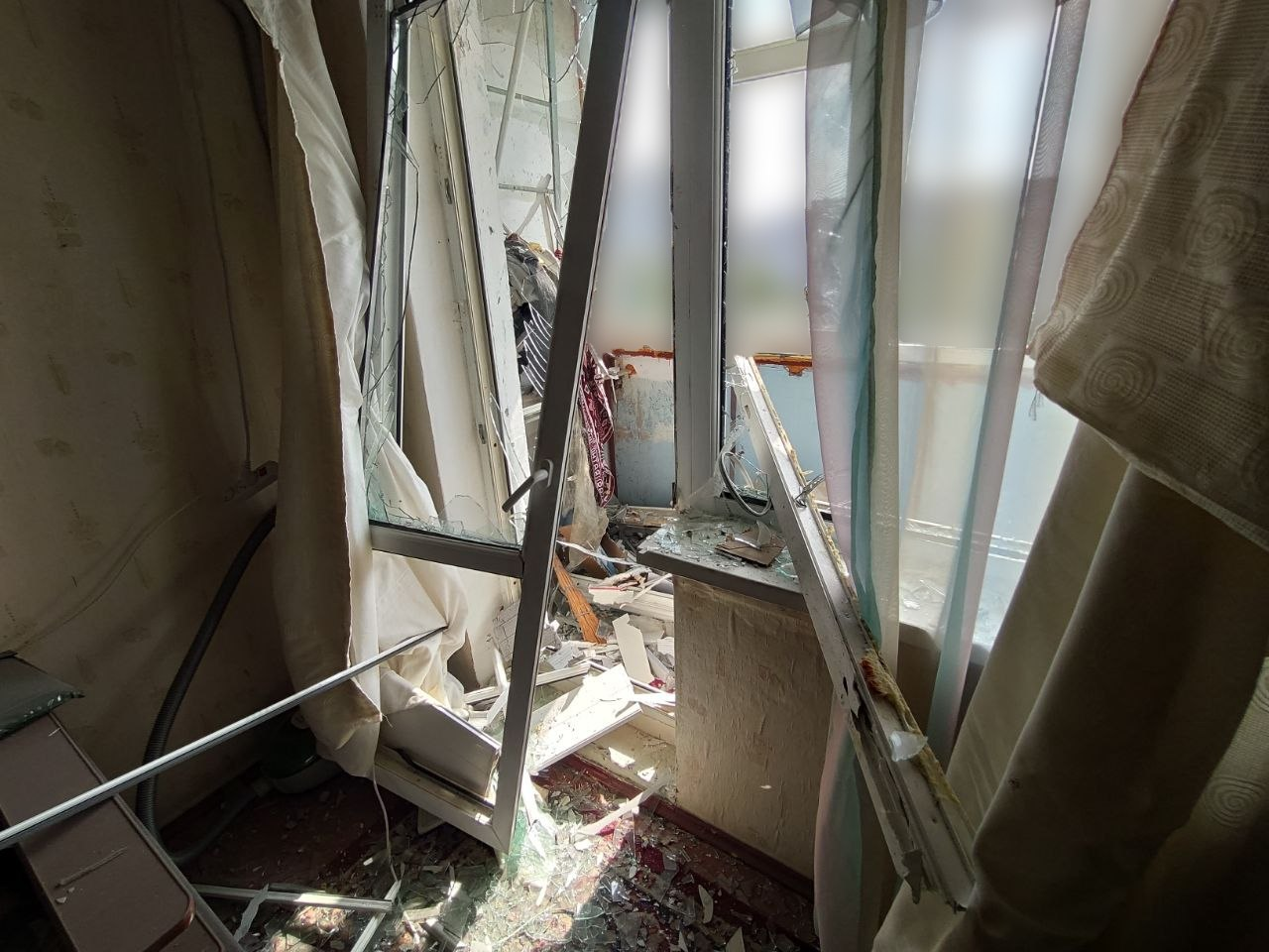 Понівечений балконний блок у квартирі багатоповерхівки в Центральному районі Херсона з вибитими шибками, деформованими пластиковими рамами та зірваними фіранками після нічного влучання російського БпЛА.