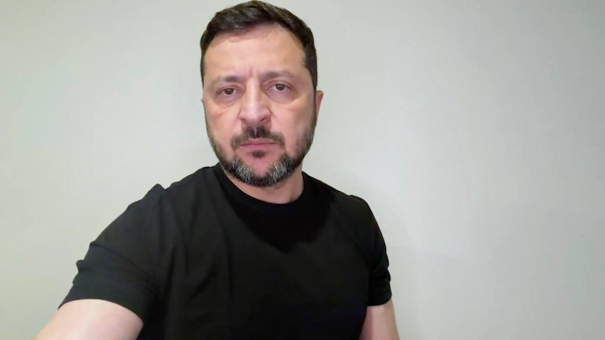 Президент Володимир Зеленський під час вечірнього відеозвернення щодо реакції України на російські удари. Глава держави у чорній футболці зафіксований на рівні грудей, дивлячись прямо в кадр із серйозним та рішучим виразом обличчя на тлі однотонної світлої стіни.