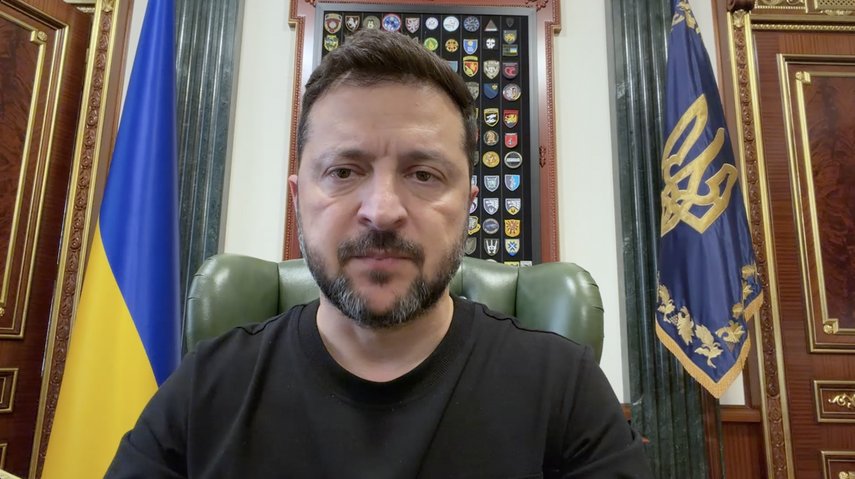 Президент України Володимир Зеленський під час офіційного відеозвернення щодо посилення українських дипстрайків для примусу Росії до миру. Голова держави зображений крупним планом у чорній футболці на тлі державних прапорів та дошки з військовими шевронами у робочому кабінеті.