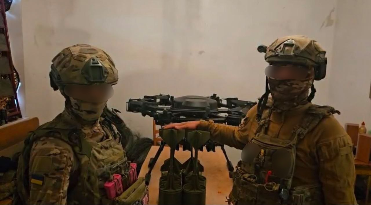 Двоє українських військовослужбовців із розмитими обличчями у повному екіпіруванні, шоломах та бронежилетах позують поруч із великим безпілотником та хвостовиками-стабілізаторами, які виготовила та передала на фронт Чулаківська СВА для підтримки Сил оборони.