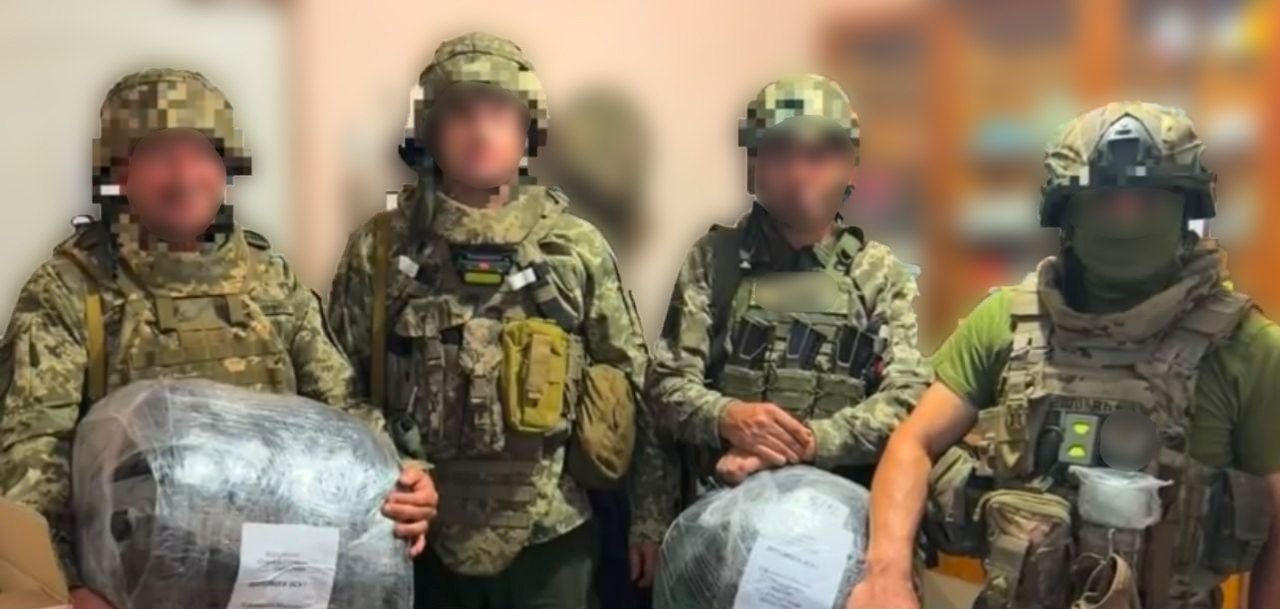 Четверо українських військовослужбовців із розмитими обличчями у військовому екіпіруванні, шоломах та бронежилетах позують у приміщенні із упакованими в плівку автомобільними шинами та технічними засобами, які передала на фронт Чулаківська СВА.
