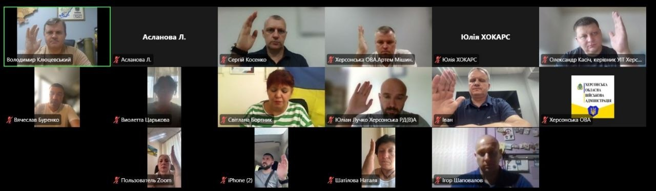 Скриншот онлайн-засідання Гуманітарного штабу при Херсонській ОВА у форматі Zoom-конференції, де учасники підняли руки під час голосування. У лівому верхньому кутку в зеленому віконці видно заступника начальника Херсонської ОВА Володимира Клюцевського, а серед інших вікон присутні: заступник начальника Херсонської РВА Юліан Лучко, директор Департаменту розвитку економіки ХОДА Артем Мішин, начальник управління інформаційних технологій ХОДА Олександр Касіч, в.о. завідувача сектору з питань запобігання та виявлення корупції Сергій Косенко та інші посадовці.