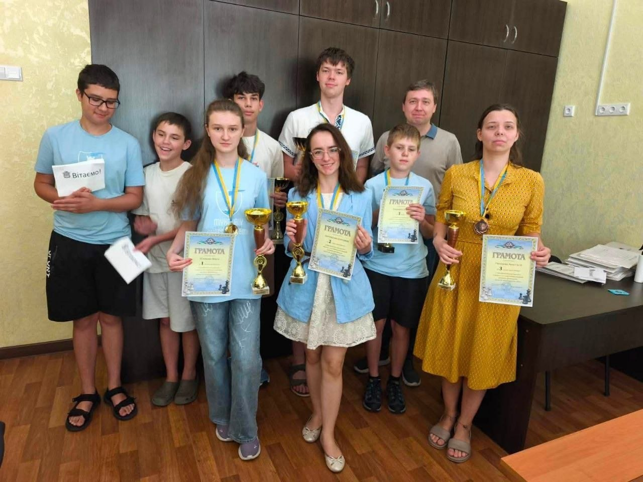 Вихованці Херсонської школи шахів разом із тренером на кваліфікаційному шаховому фестивалі «Шлях до майстерності» у Миколаєві позують із завойованими золотими кубками, медалями та грамотами за призові місця.