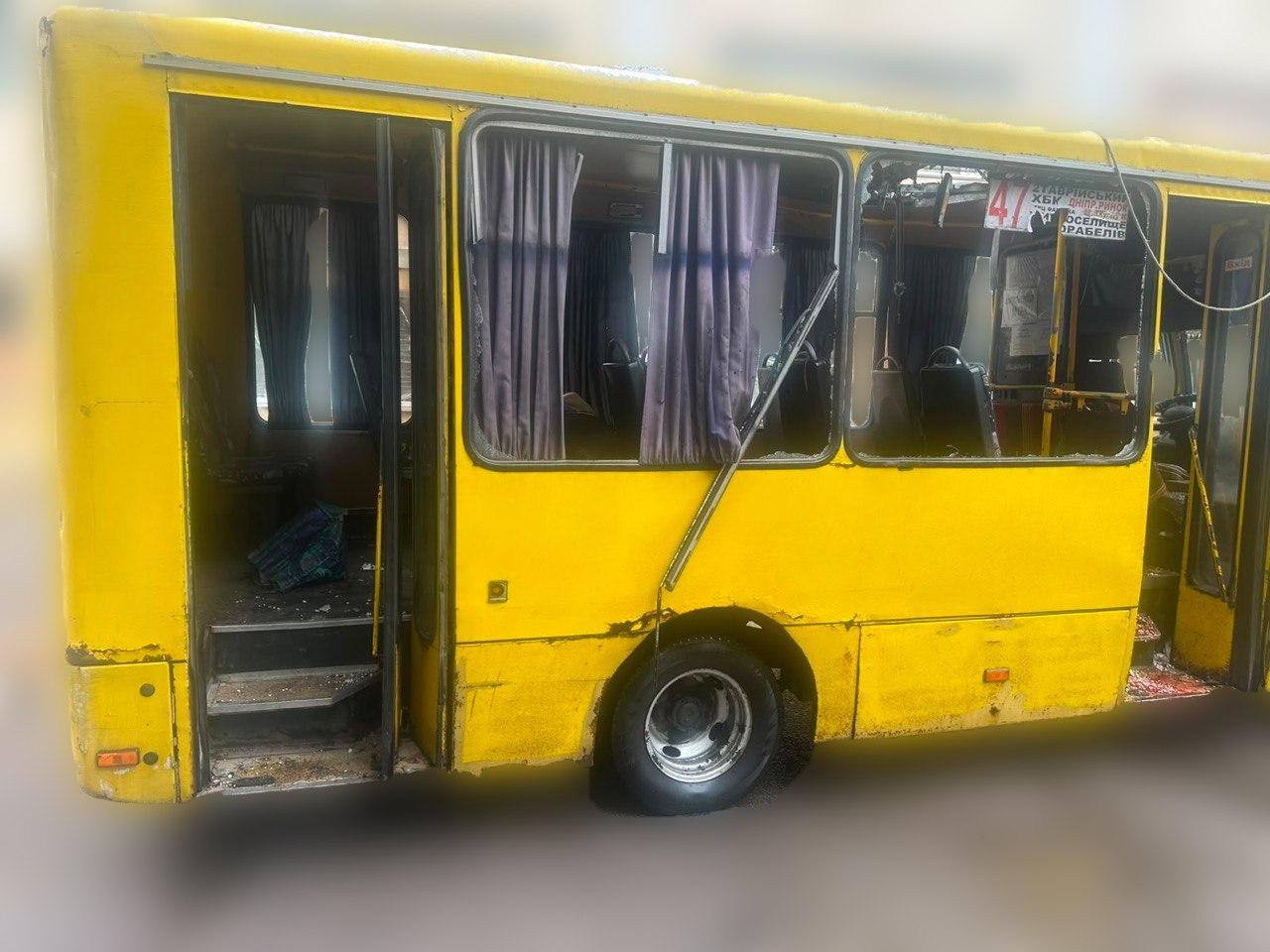 Жовтий міський автобус у Херсоні після удару російським дроном. У транспортного засобу повністю вибиті вікна, посічений кузов та відчинені двері, через які видно пошкоджений пасажирський салон із фіранками та уламками скла. На пошкодженому лобовому склі видно табличку міського маршруту №47.