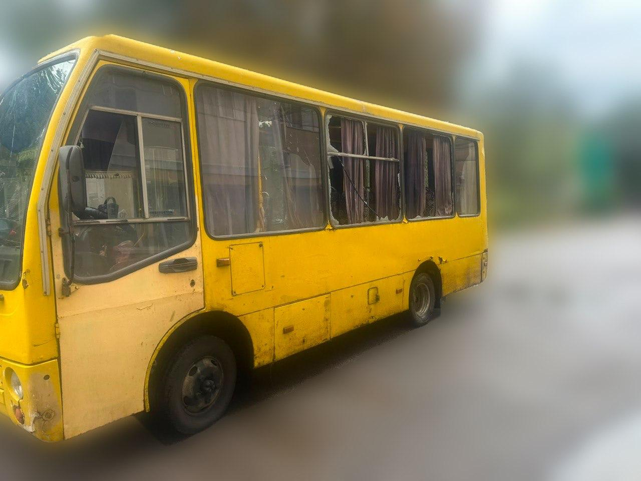 Жовтий міський автобус у Херсоні після атаки російського безпілотника, вид з лівого боку. На знімку зафіксовано масштабні руйнування скління: кілька великих пасажирських вікон повністю вибиті, всередині салону видно пошкоджені фіранки. Переднє ліве скло водія та лобове скло мають тріщини від вибухової хвилі.
