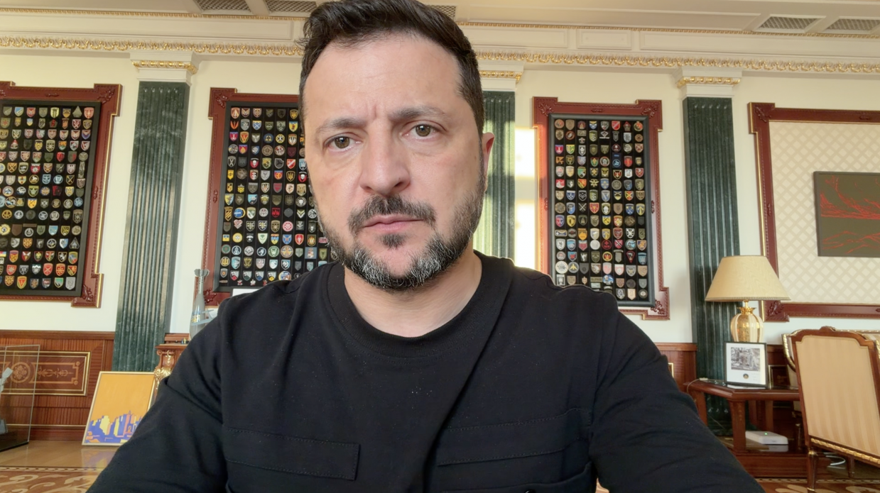 Президент України Володимир Зеленський великим планом під час звернення на тлі стіни з військовими шевронами.