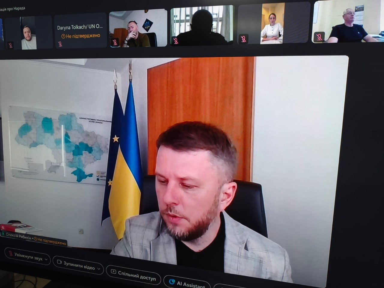 Фото екрана під час онлайн-наради на платформі відеозв'язку. На головному вікні виступає заступник Міністра розвитку громад та територій України Олексій Рябикін у світлому піджаку на тлі прапора України та великої мапи. У верхній частині екрана розміщено п'ять менших вікон інших учасників засідання, серед яких видно жінку у світлому одязі та чоловіків у кабінетах.