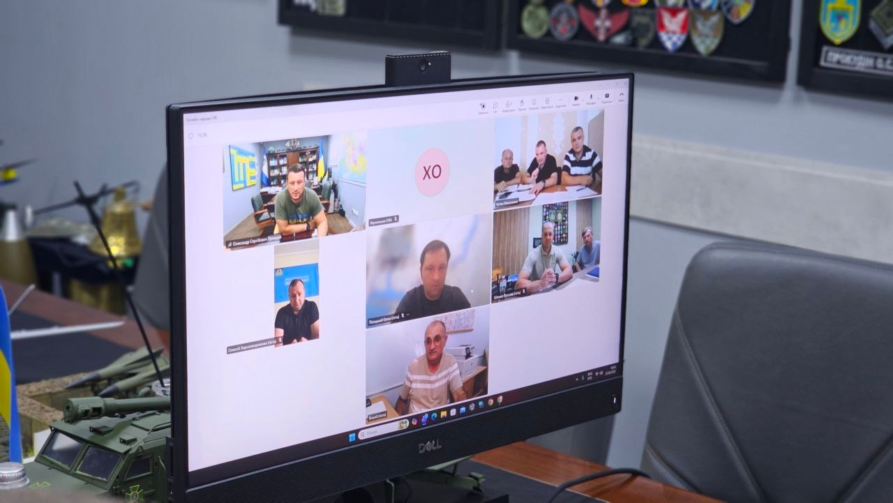 Фотографія великого монітора комп'ютера DELL, на якому відображається онлайн-нарада у форматі відеоконференції з питань відновлення критичної інфраструктури, де у лівому верхньому вікні транслюється начальник Херсонської ОВА Олександр Прокудін, у центральному середньому віконці присутній директор Департаменту з питань цивільного захисту та оборонної роботи ХОВА Євген Пісоцький, а у вікні праворуч від нього — начальник Херсонської міської військової адміністрації Ярослав Шанько, які спільно координують ліквідацію наслідків обстрілів та енергозабезпечення Пунктів Незламності.