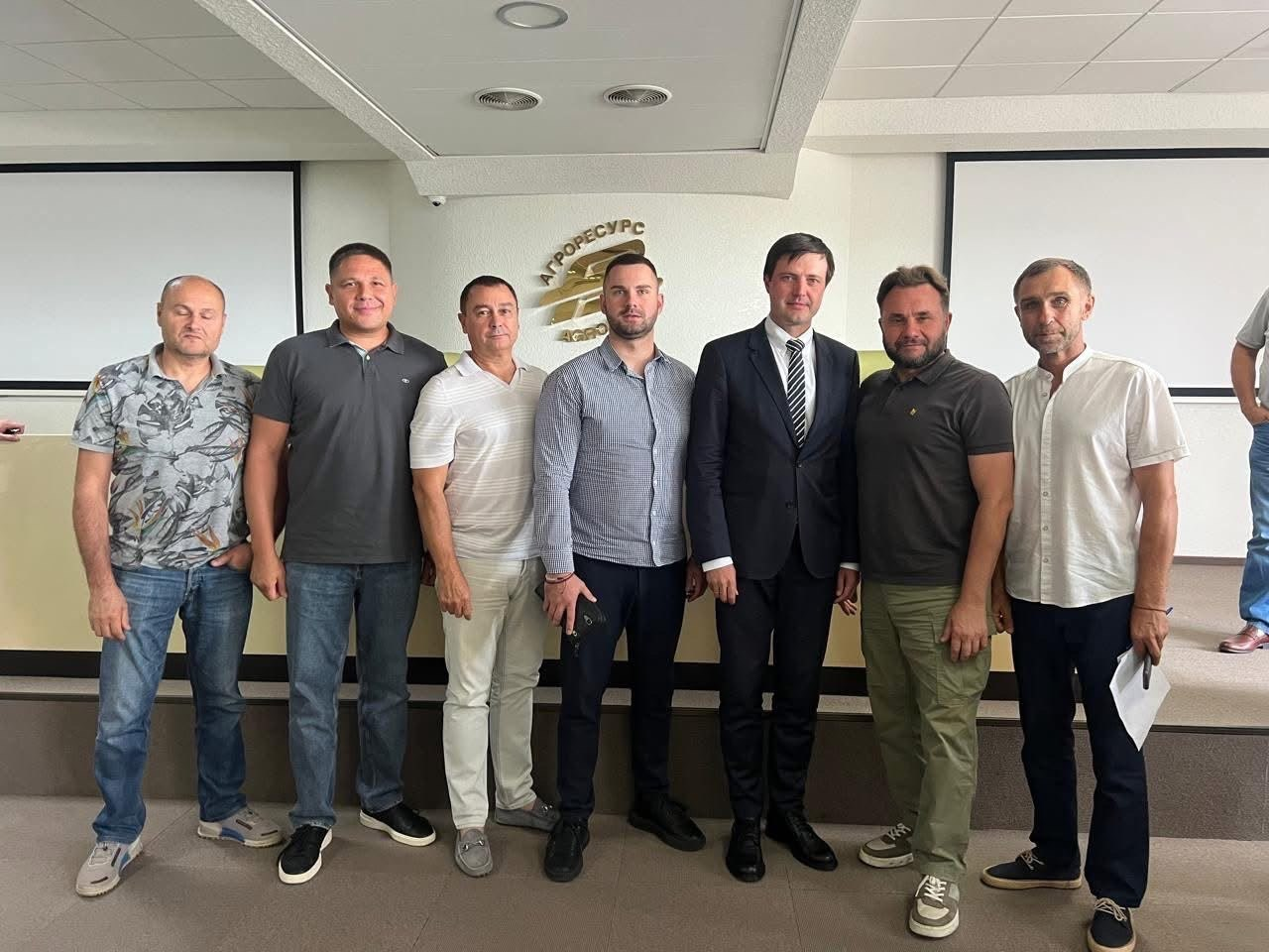 Учасники наради щодо підтримки сільгосппідприємств прифронтових територій стоять у ряд на тлі логотипа «Агроресурс» на Кіровоградщині (зліва направо): фермер Херсонщини; директор Департаменту розвитку сільського господарства та зрошення Херсонської ОДА Дмитро Юнусов; двоє представників агросектору; Міністр аграрної політики та продовольства України Тарас Висоцький; двоє аграріїв праворуч. Зустріч присвячена щоденним проблемам прифронтових господарств та державній підтримці.