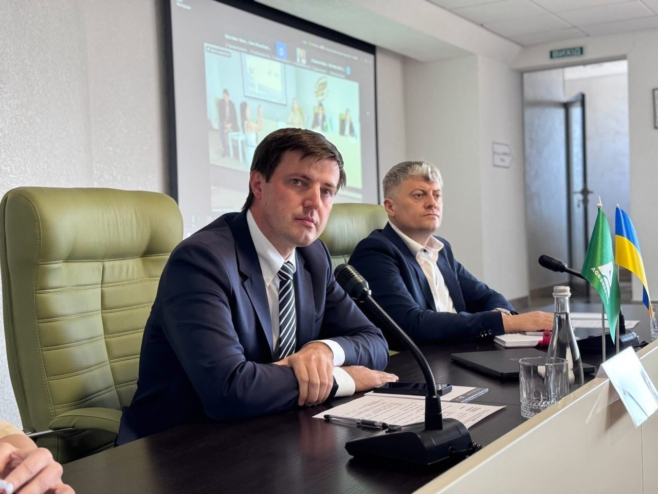 Міністр аграрної політики та продовольства України Тарас Висоцький (на передньому плані ліворуч) та перший заступник голови Кіровоградської ОВА Павло Конопко (праворуч) сидять за столом президії під час наради на Кіровоградщині щодо підтримки прифронтових сільгосппідприємств. Перед ними встановлені мікрофони та настільні прапорці України і компанії «Агроресурс», а на задньому плані видно великий екран із трансляцією учасників відеозв'язку.