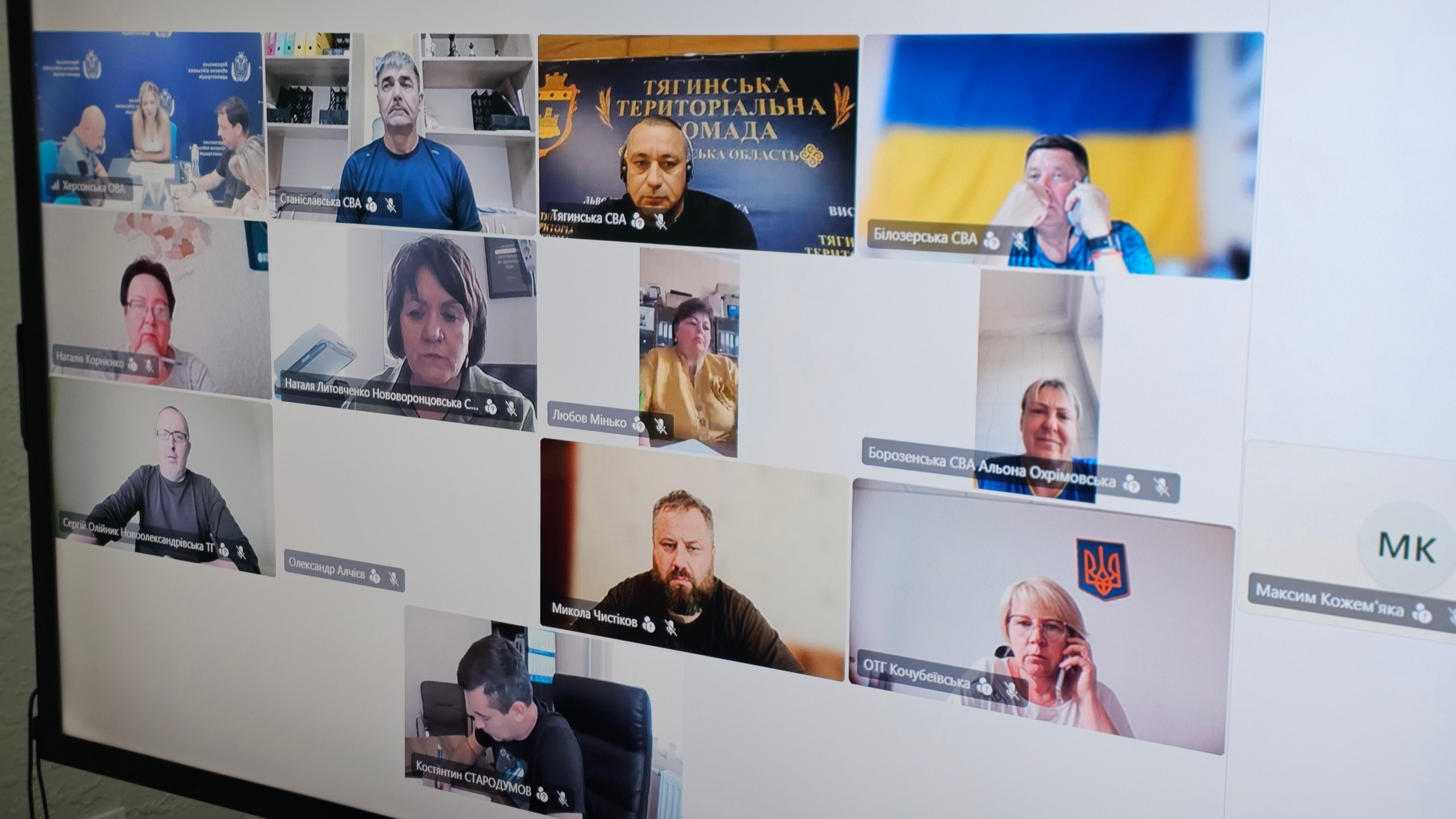 Світлина екрана монітора, на якому відображено робочу онлайн-нараду у форматі відеоконференції під головуванням заступниці начальника Херсонської ОВА Ольги Малярчук щодо захисту критичної інфраструктури деокупованих територій області. Вікно виклику поділене на сітку з трансляціями учасників. У лівому верхньому віконці видно кабінет Херсонської ОВА. Інші віконця містять трансляції керівників місцевих адміністрацій Херсонського та Бериславського районів, серед яких підписи «Станіславська СВА», «Тягинська СВА» на тлі прапора громади, «Білозерська СВА», «Наталя Литовченко Нововоронцовська С...», «Любов Мінько», «Борозенська СВА Альона Охрімовська», «Микола Чистіков», «ОТГ Кочубеївська», «Костянтин СТАРОДУМОВ» та інші. Учасники обговорюють заходи Комплексного плану стійкості області.