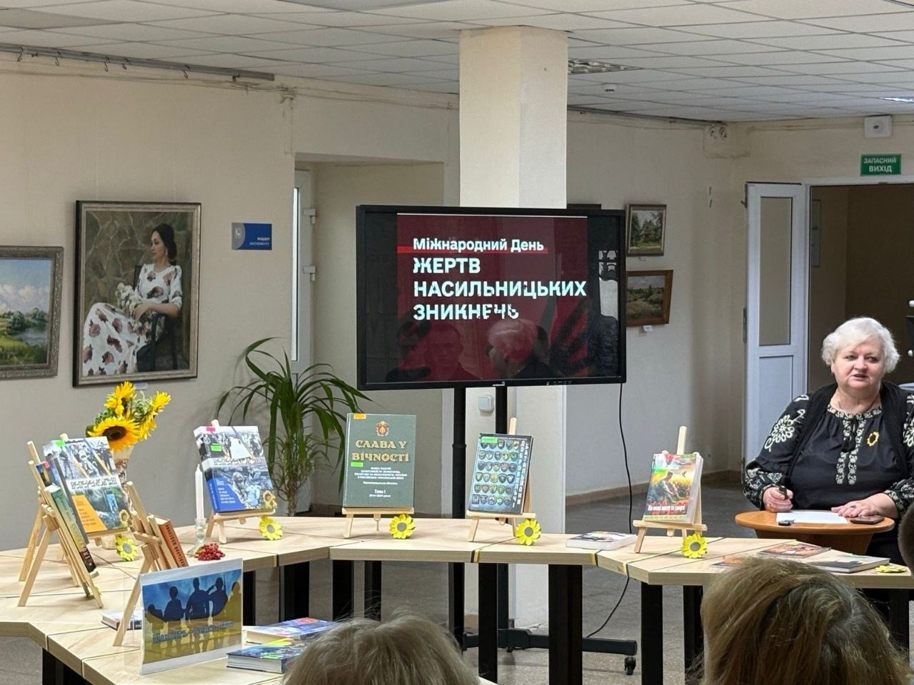Тематична інформаційно-патріотична година «За честь, за славу, за народ» для переселенців із Верхньорогачицької громади Херсонщини у Кропивницькому. Захід присвячено Дню пам'яті захисників України та Міжнародному дню жертв насильницьких зникнень. По центру залу встановлено великий екран із презентацією «Міжнародний День ЖЕРТВ НАСИЛЬНИЦЬКИХ ЗНИКНЕНЬ». Перед ним розташована книжкова виставка-меморіал, прикрашена соняшниками. Праворуч за столом сидить ведуча у вишиванці, яка розповідає про полеглих героїв та людей, зниклих безвісти внаслідок російської агресії.