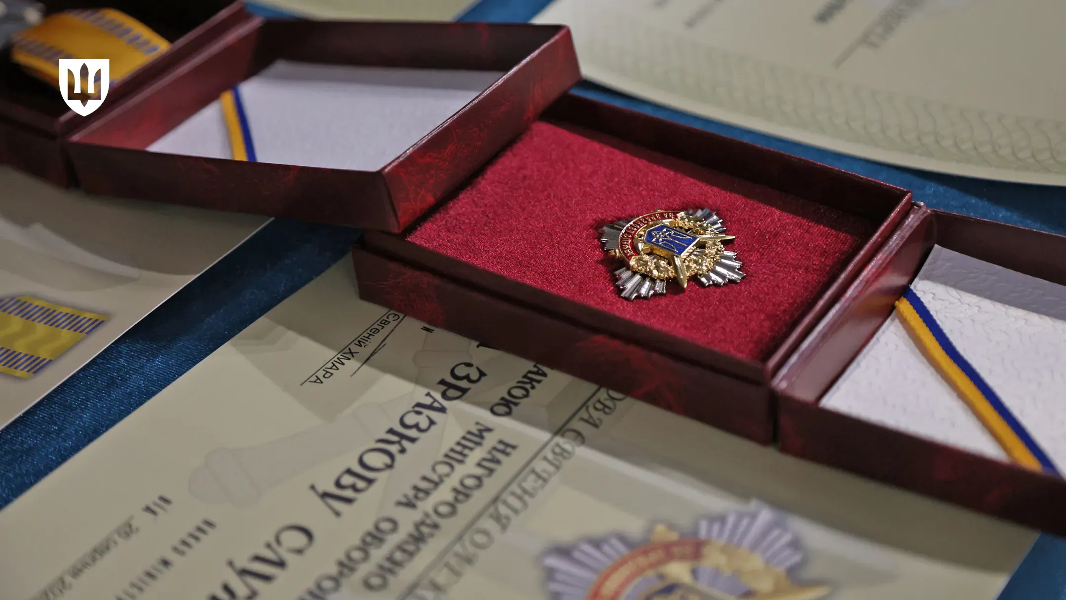 Робоча поїздка Міністра оборони України на Херсонщину. Крупний план військової відзнаки Міністерства оборони України у відкритому футлярі з темно-бордовим оксамитовим ложементом. Поруч із нагородою лежить посвідчення, на якому чітко видно частину напису «НАГОРОДЖЕНО ВІДЗНАКОЮ МІНІСТРА ОБОРОНИ „ЗА ЗРАЗКОВУ СЛУЖБУ“», а також підпис Міністра — «Євгеній ХМАРА». У лівому верхньому кутку кадру розміщено білий логотип Міністерства оборони України у формі тризуба на темному щиті.