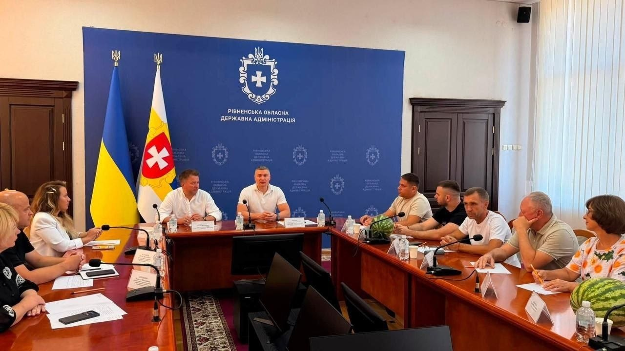 Робоча зустріч у залі засідань Рівненської обласної державної адміністрації. За великим Т-подібним дерев'яним столом сидить група людей. На задньому плані встановлено великий синій банер із гербом Рівненської області та білим написом «Рівненська обласна державна адміністрація». Ліворуч стоять два прапори: державний прапор України та офіційний прапор Рівненської області з білим хрестом на червоному щиті. У торці столу (по центру знімка) у білій футболці-поло сидить заступник голови Рівненської ОДА Олександр Кохан. Ліворуч від нього в білій сорочці сидить народний депутат України Дмитро Соломчук. Навпроти них за правою частиною столу сидить директор Департаменту розвитку сільського господарства та зрошення Херсонської ОВА Дмитро Юнусов (у світлій футболці), поруч із ним у чорній футболці — голова асоціації фермерів та приватних землевласників Херсонської області Віктор Гордієнко, а далі — інші представники агросектору Херсонщини та БФ «Жнива Перемоги». З лівого боку столу розмістилися інші учасники зустрічі. На столі перед присутніми лежать великі стиглі кавуни — символічний подарунок від херсонських аграріїв.