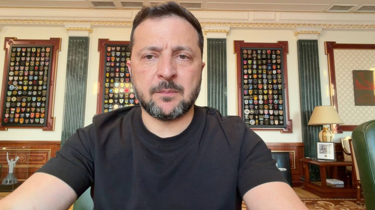 Президент України Володимир Зеленський під час відеозвернення із заявою про важливість спільних із партнерами дій у вересні задля захисту людей і миру. Голова держави у чорній футболці зафіксований крупним планом у кабінеті, на тлі стін із колекціями шевронів військових підрозділів України.