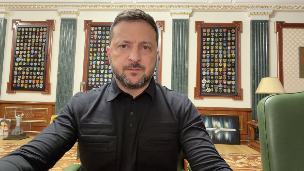 Звернення Президента України Володимира Зеленського щодо ухвалення рішень на основі домовленостей із партнерами в інтересах держави під час війни. Голова держави у чорній мілітарі-сорочці сидить у робочому кабінеті на тлі стіни з трьома великими рамками, що заповнені колекцією шевронів українських військових підрозділів. Ліворуч на столі стоїть мініатюрний макет монумента «Батьківщина-мати».