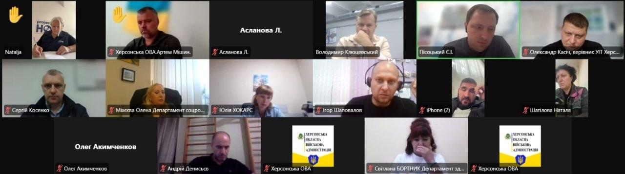 Скриншот онлайн-наради в режимі відеоконференції демонструє чергове засідання Гуманітарного штабу при Херсонській ОВА під головуванням заступника голови Херсонської ОДА Володимира Клюцевського. Вікно трансляції розділене на сітку з віконець учасників, де у верхньому ряду присутні заступник голови Херсонської ОДА Володимир Клюцевський, директор Департаменту розвитку економіки ХОДА Артем Мішин та начальник управління інформаційних технологій ХОДА Олександр Касіч. У середньому й нижньому рядах обговорення та погодження допомоги для громад ведуть директор Департаменту соціального захисту ХОДА Олена Міхєєва та інші посадовці: Сергій Косенко, Ігор Шаповалов, Андрій Денисьєв, Світлана Бортник. Кілька віконець відображають текстові імена або офіційний логотип із написом «ХЕРСОНСЬКА ОБЛАСНА ВІЙСЬКОВА АДМІНІСТРАЦІЯ», а підключені фахівці узгоджують виділення генераторів, пального та техніки для адаптивного спорту.