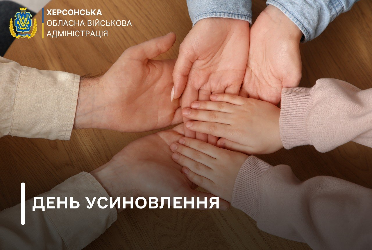 Офіційний банер Херсонської обласної військової адміністрації до Дня усиновлення, на якому крупним планом зображено руки родини, що складені одна на одну на тлі світлої дерев'яної поверхні. Внизу розташовані великі відкриті долоні дорослих, на яких ніжно лежать дві маленькі дитячі долоньки, що символізує єдність, турботу та родинне тепло. У лівому верхньому кутку банера розміщено кольоровий герб та офіційний напис «ХЕРСОНСЬКА ОБЛАСНА ВІЙСЬКОВА АДМІНІСТРАЦІЯ», а в лівому нижньому кутку великими білими літерами після вертикальної лінії нанесено заголовок «ДЕНЬ УСИНОВЛЕННЯ»