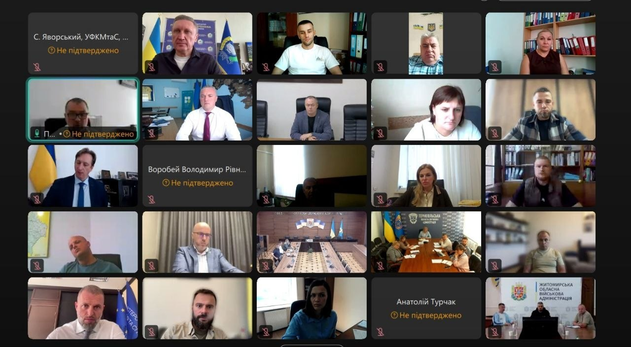 Скриншот онлайн-наради у форматі відеоконференції під час засідання Організаційного комітету всеукраїнських шкільних та студентських ліг «Пліч-о-пліч». На екрані відображено велику сітку з 25 квадратними віконцями, у яких присутні учасники зустрічі, представники регіональних адміністрацій та спортивних відомств, які обговорюють організаційне забезпечення змагань і розвиток учнівського й студентського спорту. Окремі учасники виходять на зв'язок на тлі державних прапорів України, робочих кабінетів, офіційних банерів із символікою (зокрема Житомирської ОВА у правому нижньому кутку), тоді як частина вікон містить текстові заставки з іменами або повідомлення про відсутність підтвердження трансляції.
