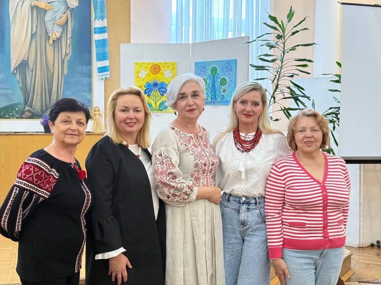 П'ять жінок урочисто стоять у ряд і посміхаються в камеру під час презентації родинного проєкту майстрів із тимчасово окупованої Херсонщини Інни Красновської-Кафтан та Миколи Кафтана «Чари степового краю», яку в межах організації дозвілля для переселенців відвідали херсонці завдяки Координаційному центру «Вільні разом» в Івано-Франківську. Зліва направо вишикувалися: жінка у чорній вишиванці з червоно-білим геометричним орнаментом, жінка у чорному піджаку, жінка зі світлим каре у довгій лляній сукні з вишивкою, блондинка у білій вишиванці, великому червоному намисті та світло-блакитних джинсах, а також жінка праворуч у смугастій рожево-білій кофті та синіх джинсах. Воя стоять у залі на тлі виставкових робіт із патріотичними мотивами, великої картини із зображенням Богородиці з немовлям, вишитого рушника та великої кімнатної рослини.
