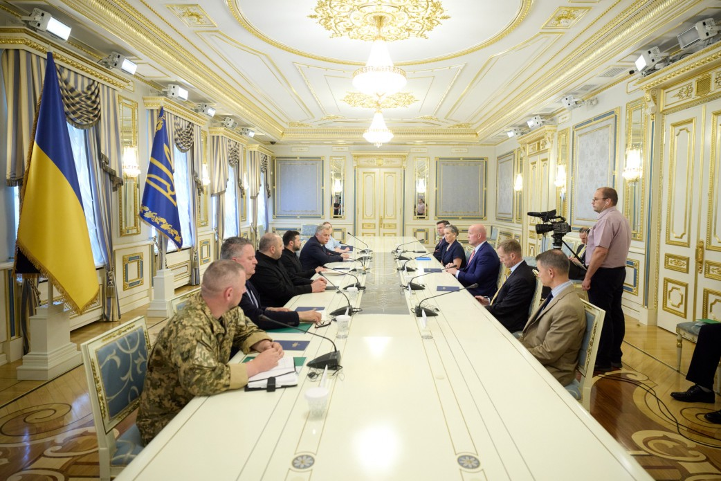 Президент України Володимир Зеленський та Посол США при НАТО Метью Вітакер разом із делегаціями проводять офіційну зустріч за довгим столом у розкішній залі засідань, обговорюючи захист українського неба та ліцензії на виробництво ракет для систем Patriot. З лівого боку столу сидить українська сторона на чолі з Главою держави, а навпроти них розмістилися американські партнери, серед яких генерал-лейтенант Кертіс Баззард. Кадр відображає процес важливого міжнародного діалогу щодо результатів саміту НАТО в Анкарі, роботи над угодою у форматі Drone Deal та розвитку програми фінансування оборонного спорядження PURL на суму близько 8 мільярдів доларів.