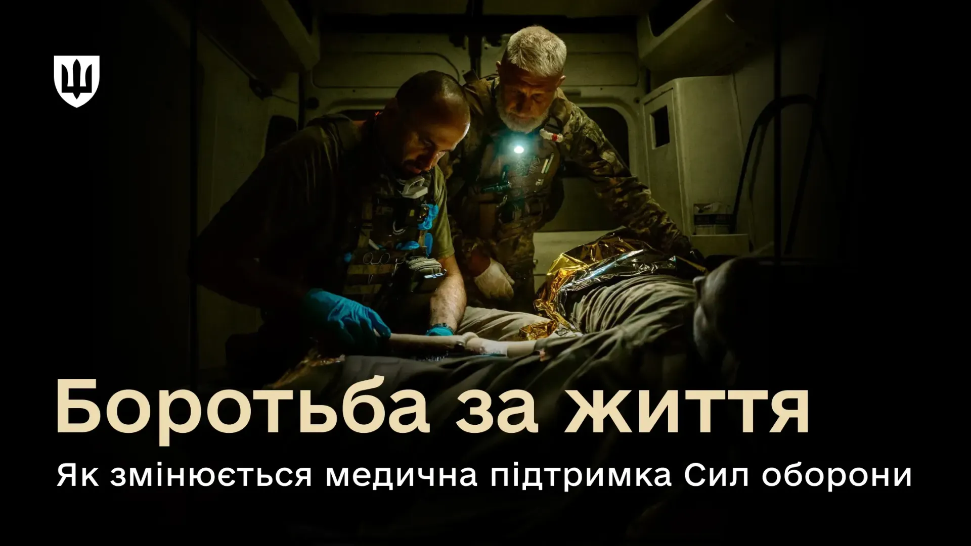 Офіційний інформаційний банер до Дня медичного працівника із заголовком про розвиток військової медицини, на якому зафіксовано надання невідкладної тактичної допомоги пораненому бійцю всередині евакуаційного автомобіля. В умовах обмеженого нічного освітлення двоє військових медиків у захисному спорядженні схилилися над пораненим, який лежить на ношах під термоковдрою. Один фахівець у блакитних гумових рукавичках обережно накладає пов'язку, а другий, із налобним ліхтариком, контролює стан пацієнта. У лівому верхньому кутку розміщено білий Малий Державний Герб України, а внизу нанесено великий напис «Боротьба за життя. Як змінюється медична підтримка Сил оборони», що ілюструє масштабне оновлення системи від Міноборони: затвердження стандартів НАТО для тимчасових формувань Role 1 та Role 2, оновлення Воєнно-медичної доктрини, легалізацію знеболення на фронті, курси для хірургів Storm 2 та отримання 400 000 якісних аптечок IFAK від Німеччини.