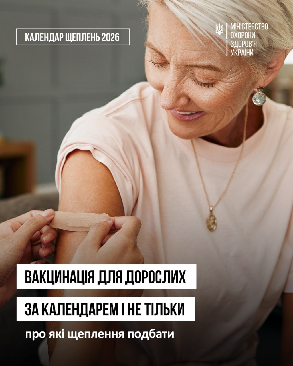 Офіційний інформаційний банер Міністерства охорони здоров'я України із заголовком про вакцинацію, на якому зображено жінку старшого віку, котрій на плече наклеюють медичний пластир після проведення щеплення. Жінка у ніжно-рожевій футболці посміхається, спостерігаючи за руками медика, а на плакаті розміщено логотип МОЗ України з тризубом, напис «КАЛЕНДАР ЩЕПЛЕНЬ 2026» та головний заголовок «ВАКЦИНАЦІЯ ДЛЯ ДОРОСЛИХ ЗА КАЛЕНДАРЕМ І НЕ ТІЛЬКИ». Кадр ілюструє роз'яснення щодо необхідності оновлення захисту протягом усього життя, зокрема безоплатної ревакцинації проти дифтерії та правця щодесять років, щорічних щеплень проти грипу та COVID-19, а також рекомендованої імунізації для дорослих проти гепатитів А і B, вірусу папіломи людини (ВПЛ) та кашлюку.