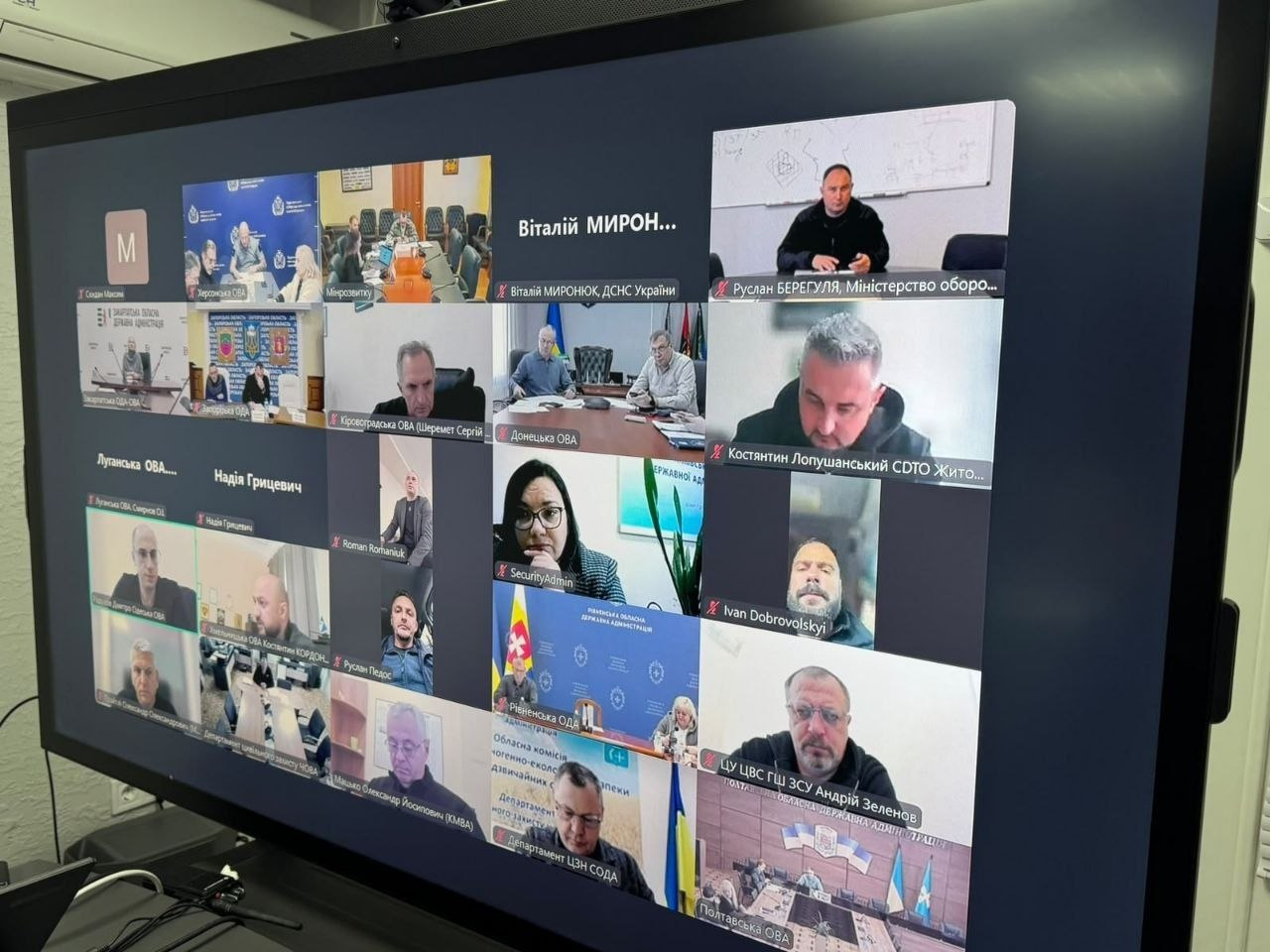 На екрані великого монітора в інтерфейсі онлайн-платформи зафіксовано масштабну робочу зустріч Координаційного штабу з проведення евакуаційних заходів під головуванням Міністра у справах громад, територій та внутрішньо переміщених осіб України Віталія Безгіна. Вікно відеодзвінка розділене на велику кількість інтерактивних віконець, де у правому верхньому кутку доповідає начальник Департаменту екологічної безпеки та протимінної діяльності Міністерства оборони України Руслан Берегуля, трохи нижче по центру праворуч сидить заступник начальника Житомирської ОВА Костянтин Лопушанський (CDTO), а в нижньому правому секторі відображається вікно ЦУ ЦВС ГШ ЗСУ Андрія Зеленова. Також серед чисельних учасників наради у сітці присутні представники Донецької, Луганської, Рівненської, Полтавської, Кіровоградської обласних військових адміністрацій та Управління цивільно-військового співробітництва, що ілюструє процес обговорення підготовки транзитного центру в Миколаєві, залучення гуманітарного простору «Вільні разом» та узгодження алгоритмів постійної евакуації родин із дітьми з прифронтових територій в осінньо-зимовий період.