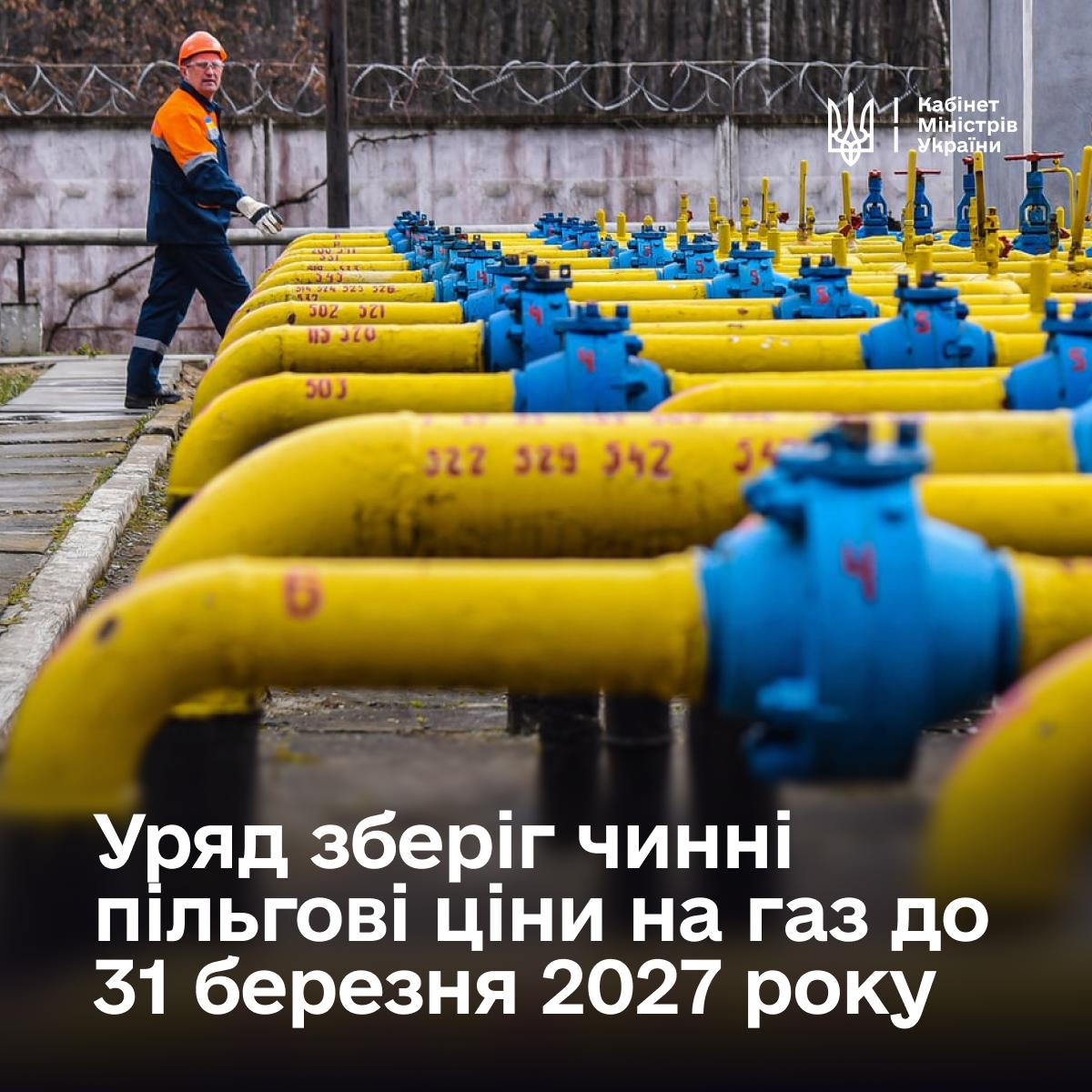 Офіційний інформаційний банер Кабінету Міністрів України, який інформує про продовження дії пільгових тарифів на блакитне паливо для населення та виробників тепла, виконаний у стилістиці промислового кадру газорозподільної станції. У правому верхньому кутку розміщено малий Державний Герб України (Тризуб) та офіційний підпис «Кабінет Міністрів України». Головним планом зображено численні довгі жовті газові труби з синіми запірними вентилями та маркуванням цифр, що простягаються рядами вздовж усього майданчика. Ліворуч на задньому плані вздовж бетонного паркану з колючим дротом крокує робітник підприємства у темно-синьому робочому костюмі зі світловідбивними помаранчевими елементами, захисній касці та окулярах. У нижній частині банера нанесено великий чіткий білий напис: «Уряд зберіг чинні пільгові ціни на газ до 31 березня 2027 року», що відображає рішення про стабільність тарифів на час воєнного стану та опалювального сезону.