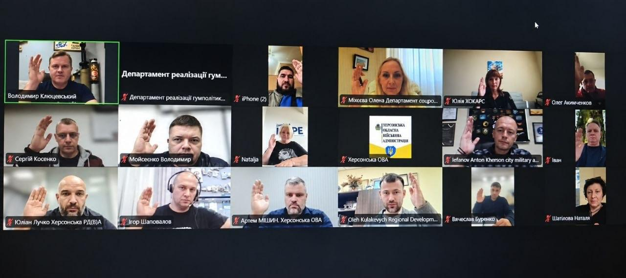 Екран монітора відображає велику сітку вікон онлайн-зв'язку програми Microsoft Teams під час голосування на засіданні гуманітарного штабу ХОВА під головуванням заступника начальника Херсонської ОДА Володимира Клюцевського. Численні учасники наради синхронно підняли руки на знак підтримки рішень, причому у лівому верхньому кутку в зеленому віконці транслюється сам Володимир Клюцевський. Серед інших підключених вікон присутні: перший заступник начальника Херсонської МВА Михайло Линецький, заступник начальника Херсонської МВА Антон Єфанов, директор «Агенції регіонального розвитку “Офіс євроінтеграції” Херсонської області» Олег Кулакевич, директор Департаменту розвитку економіки Херсонської ОДА Артем Мішин, директорка Департаменту соціального розвитку Херсонської ОДА Олена Міхєєва, начальник управління з питань децентралізації та розвитку громад Херсонської ОДА Юліан Лучко, начальник юридичного відділу Херсонської ОДА Володимир Мойсеєнко та інші учасники наради. Кадр ілюструє процес дистанційного ухвалення рішень щодо забезпечення медичних закладів резервним живленням і водою, а також підтримки безперебійної роботи системи оповіщення у Херсоні.