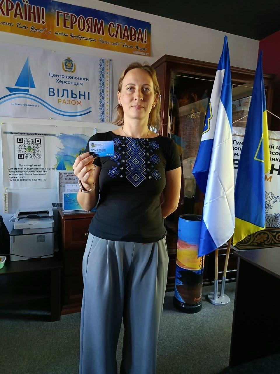 Переселенка з Херсонщини тримає в руці отриману «Картку Херсонщини» в координаційному центрі «Вільні разом» в Івано-Франківську, де вона одягнена в чорну футболку з блакитним вишитим орнаментом та сірі штани і позує на тлі символіки хабу, зокрема великого плаката ліворуч із написом «Центр допомоги херсонцям ВІЛЬНІ РАЗОМ м. Івано-Франківськ», банера «Карта Херсонщини Вільні Разом» із QR-кодами, а праворуч від неї на підставках стоять Державний прапор України та прапор Херсонської області, причому над плакатами зверху закріплено патріотичне гасло «УКРАЇНІ! ГЕРОЯМ СЛАВА!».