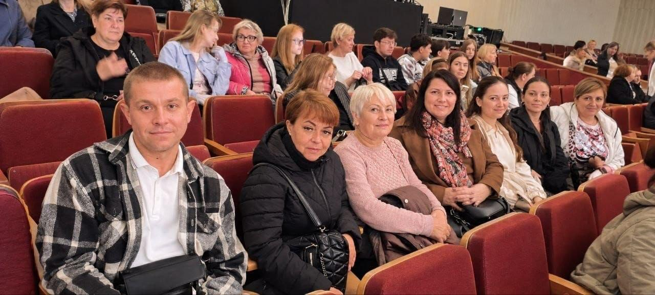 Координаційний центр «Вільні разом» у Житомирі організував культурне дозвілля для переселенців із Херсонщини, які відвідали концерти Анни Буткевич у Телецентрі та ансамблю «Льонок» у Житомирській обласній філармонії. На світлині зафіксовані херсонські глядачі, які сидять у залі на м'яких бордових кріслах в очікуванні початку виступу. На передньому плані ліворуч сидить чоловік у чорно-білій клітчастій сорочці-жакеті, поруч із яким розмістився ряд жінок в осінніх куртках, пальтах та светрах, а на задніх рядах помітно інших відвідувачів. Такі безкоштовні мистецькі заходи допомагають внутрішньо переміщеним родинам покращити психоемоційний стан в евакуації та долучитися до культурного життя Житомирщини.