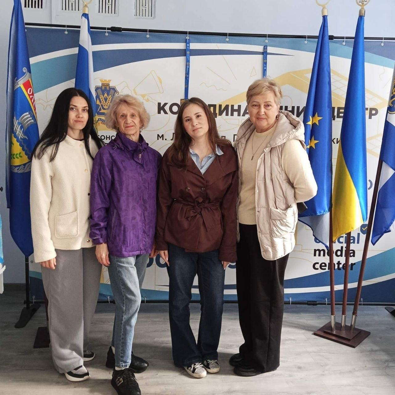 На світлині у повний зріст зображено чотирьох жінок, які стоять у приміщенні Львівського координаційного центру «Вільні разом» на тлі офіційного банера та прапорів. Якщо дивитися від правого краю до лівого, перша жінка з короткою світлою зачіскою одягнена у світло-бежеву безрукавку поверх кофти та чорні штани. Поруч із нею стоїть дівчина у коричневому плащі, блакитній сорочці у смужку, темних джинсах та кедах. Третя жінка зі світлим волоссям одягнена у фіолетову куртку та світло-сині джинси, а четверта учасниця ліворуч — у світлу трикотажну кофту на ґудзиках та вільні сірі штани. Позаду жінок розміщено великий синьо-білий банер із написом «КООРДИНАЦІЙНИЙ ЦЕНТР...» та англійським текстом «Social media center» у нижньому кутку. Праворуч на металевих стійках встановлено три великі прапори, серед яких Державний Прапор України та синій прапор Європейського Союзу, а ліворуч за спинами жінок видно синій прапор Херсонської області.
