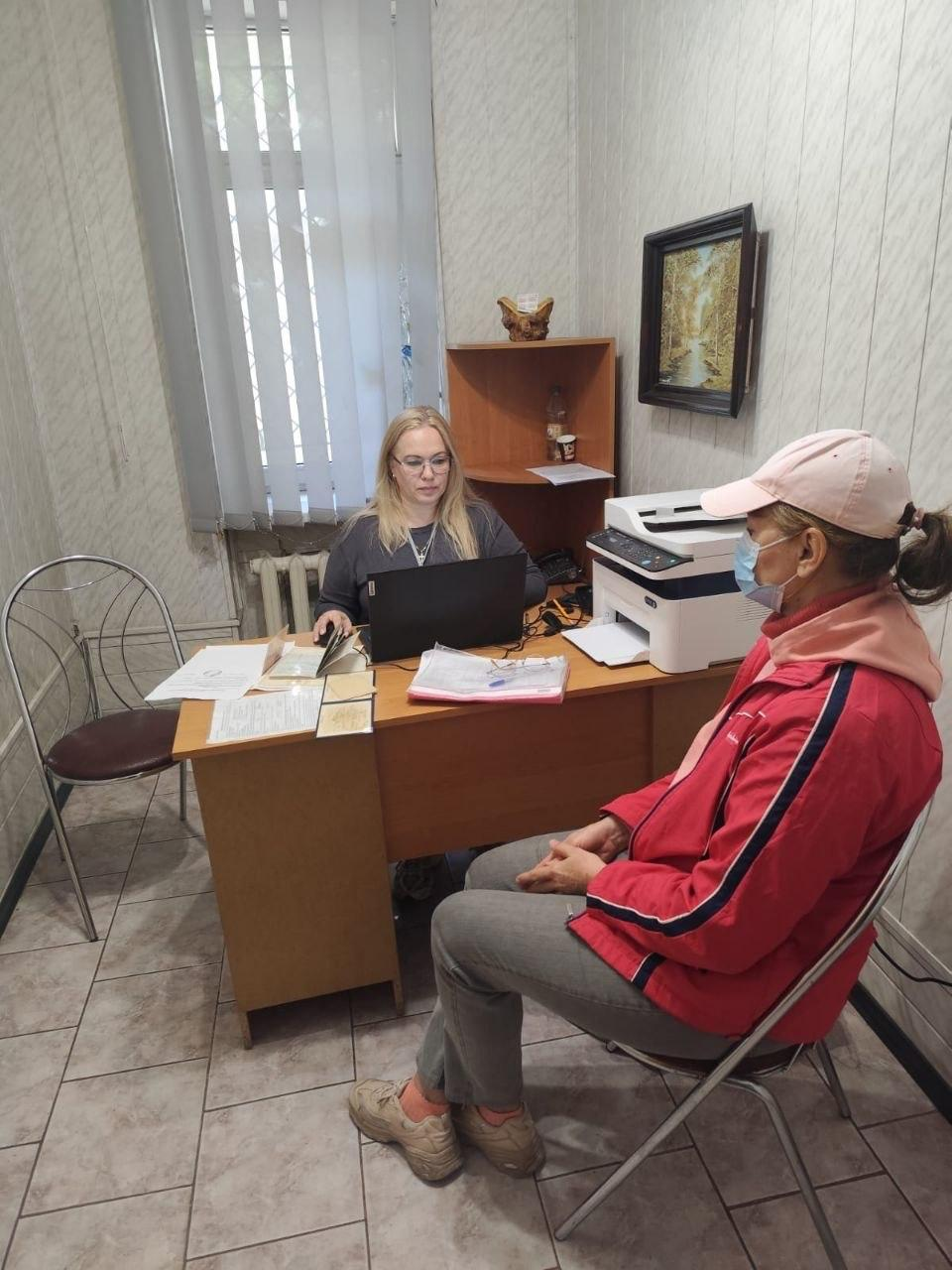 На світлині зафіксовано робочий момент надання юридичної допомоги внутрішньо переміщеним особам з Херсонщини в Одеському координаційному центрі «Вільні разом». У кабінеті з кахельною підлогою та світлими стінами за дерев'яним столом сидить юристка в окулярах та темній кофті, яка консультує відвідувачку та працює за чорним ноутбуком фірми Lenovo. Перед фахівчинею на столі розкладено робочі папери, бланки та розгорнутий паспорт громадянина України, а праворуч на краю столу встановлено великий білий принтер. Навпроти неї на стільці боком до об'єктиву сидить жінка-переселенка у рожевій кепці, захисній медичній масці, червоній спортивній куртці з білою смугою на рукаві та сірих штанях, яка уважно слухає роз'яснення. Інтер'єр кімнати доповнюють кутова дерев'яна полиця на задньому плані, картина у темній рамці на стіні та велике вікно з вертикальними жалюзі.