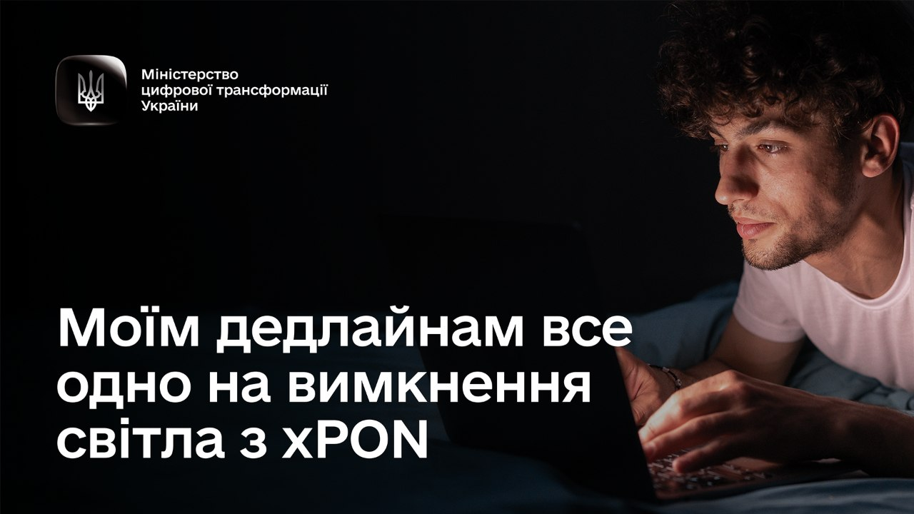 На світлині зображено офіційний рекрутинговий або інформаційний плакат від Міністерства цифрової трансформації України, присвячений перевагам енергонезалежного інтернету за технологією xPON. Ліворуч на суцільному темному фоні великими білими літерами нанесено гасло: «Моїм дедлайнам все одно на вимкнення світла з xPON». У лівому верхньому кутку плаката розміщено квадратний логотип міністерства із Державним Гербом України та білим текстом «Міністерство цифрової трансформації України». Праву частину кадру займає фотографія молодого кучерявого чоловіка у білій футболці, обличчя якого в темряві кімнати яскраво освітлюється лише знизу екраном ноутбука, на клавіатурі якого лежать його руки під час роботи.