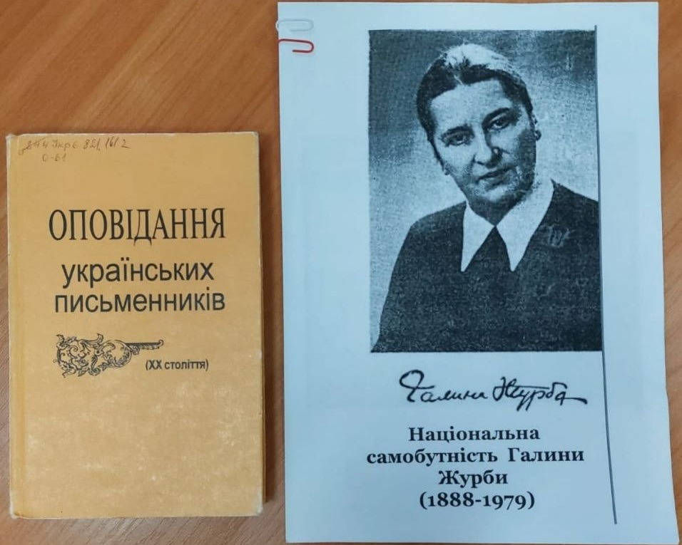 На світлині крупним планом зображено друковані матеріали до літературної зустрічі, що присвячена творчості української письменниці. Ліворуч лежить стара книга у жовтій твердій обкладинці з написом «ОПОВІДАННЯ українських письменників (ХХ століття)», на якій зверху помітні бібліотечні індекси, нанесені олівцем. Праворуч розташовано роздрукований аркуш паперу білого кольору із чорно-білим портретом Галини Журби. Під її фотографією міститься графічний факсимільний підпис авторки, а нижче нанесено друкований заголовок: «Національна самобутність Галини Журби (1888-1979)». Матеріали розкладені поруч на коричневій дерев'яній поверхні столу.