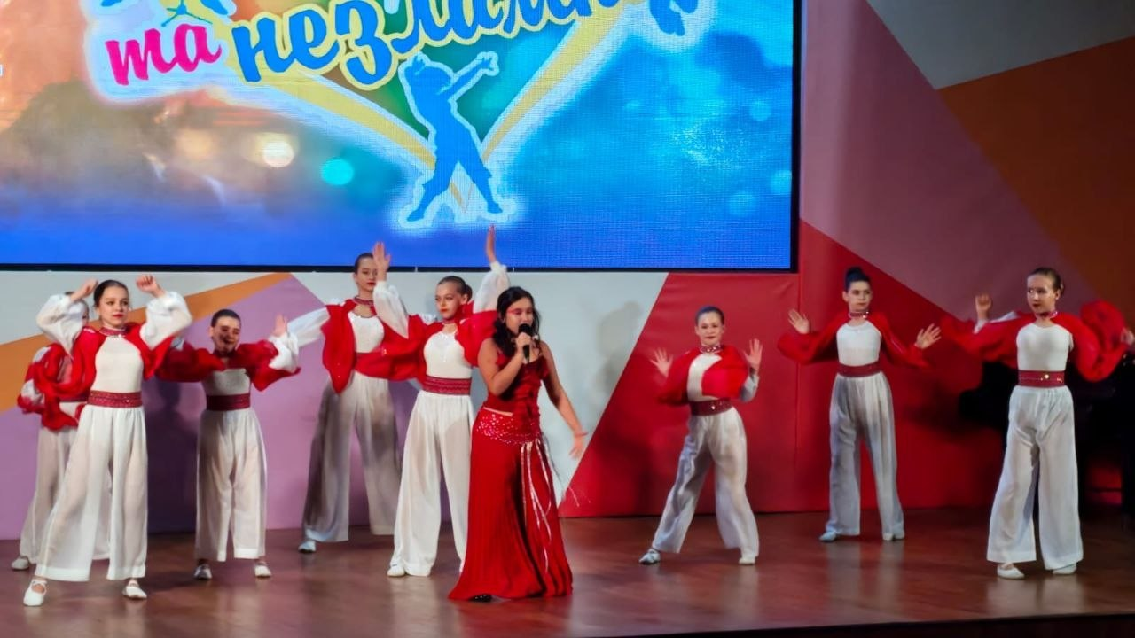 На сцені у Миколаєві під час Міжнародного багатожанрового фестивалю «Талановиті та незламні», організованого Херсонським обласним палацом культури за підтримки Департаменту реалізації гуманітарної політики Херсонської ОДА, виступає творчий колектив дівчат. У центрі сцени співає солістка в довгій червоній сукні з мікрофоном у руці, а позаду та обабіч неї танцюють учасниці в автентичних стилізованих костюмах — широких білих шароварах, білих блузах та яскраво-червоних накидках-болеро з широкими рукавами. Ззаду на великому світлодіодному екрані відображається частина яскравого банера проєкту з написом «Талановиті та незламні» та силуетом дівчини, що танцює. Цей художній номер є частиною концертної програми, яка об'єднала понад 300 виконавців задля збереження українських культурних традицій та представлення творчості митців півдня країни.