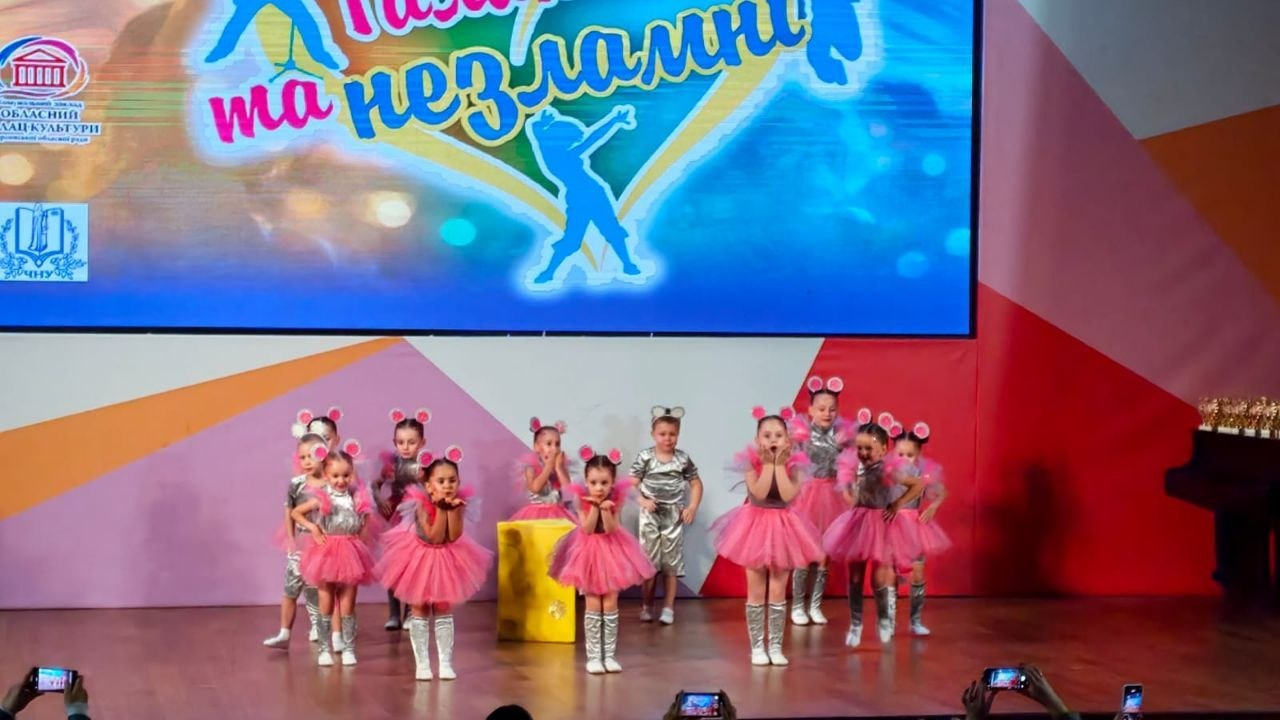 На сцені у Миколаєві під час Міжнародного багатожанрового фестивалю «Талановиті та незламні», організованого Херсонським обласним палацом культури за підтримки Департаменту реалізації гуманітарної політики Херсонської ОДА, виступає наймолодша група учасників. На сцені танцює дитячий хореографічний колектив малюків у яскравих костюмах мишенят — дівчатка в пишних рожевих пачках і сріблястих топах та один хлопчик у сірому комбінезоні, у всіх на головах обручі з кумедними вушками. По центру стоїть декорація у вигляді великого шматка сиру, а діти емоційно виконують постановку перед глядачами, які знімають дійство на мобільні телефони. Ззаду на великому світлодіодному екрані відображається банер проєкту з написом «Талановиті та незламні» та силуетом дівчини, що танцює. Цей яскравий дитячий номер є частиною святкової програми, яка об'єднала понад 300 виконавців задля збереження українських культурних традицій та представлення творчості митців півдня країни.