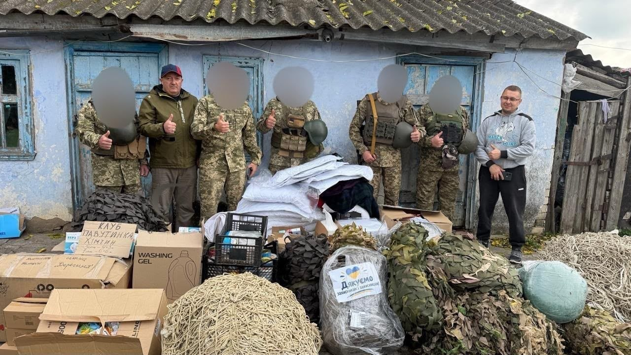 Зустріч волонтерів та керівництва Чулаківської громади з українськими військовими під час передачі гуманітарної допомоги: на передньому плані перед старою одноповерховою будівлею з блакитними стінами розкладено велику кількість допомоги — картонні коробки (зокрема з підписами клубу «Павутинка» та спільноти «Берегиня»), пластикові ящики, стопки теплих речей та великі рулони білих, зелених і коричневих маскувальних сіток, на одній з яких закріплено папірець із написом «Дякуємо захисникам і захисницям!», а на задньому плані в один ряд стоять семеро людей, серед яких п'ятеро військовослужбовців ЗСУ у камуфляжній формі та бронежилетах (їхні обличчя приховані цифровим розмиттям з міркувань безпеки), начальник Чулаківської СВА Руслан Русаль у коричнево-зеленій куртці та кепці (другий ліворуч) та молодий чоловік у сірому спортивному худі (праворуч), причому більшість присутніх тримають великі пальці піднятими вгору.